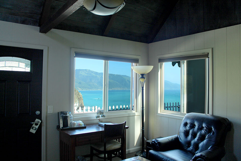 Bed with ocean and mountain view through the window of an Oceanview Luxury cabin at Lucia Lodge
